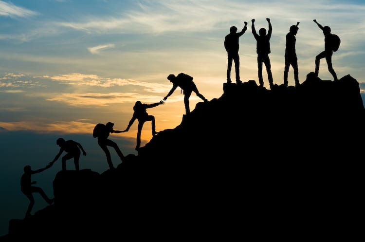 People helping each other and celebrating reaching the top of the mountain.